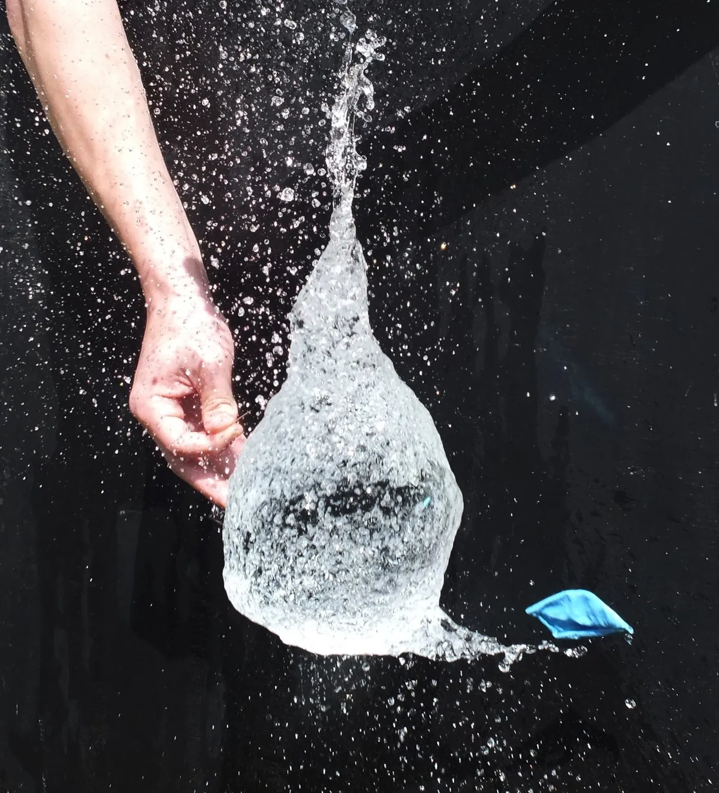 Water Balloon Burst: Frozen mid-burst as a pin pops it, against a black backdrop.